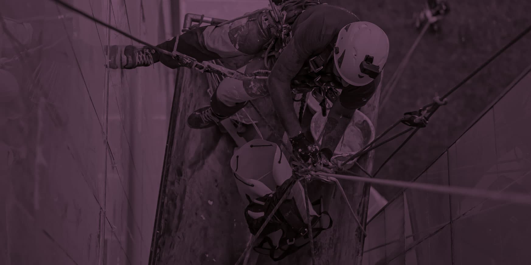 A worker in safety gear rappels down a building, using ropes and harnesses, viewed from above.